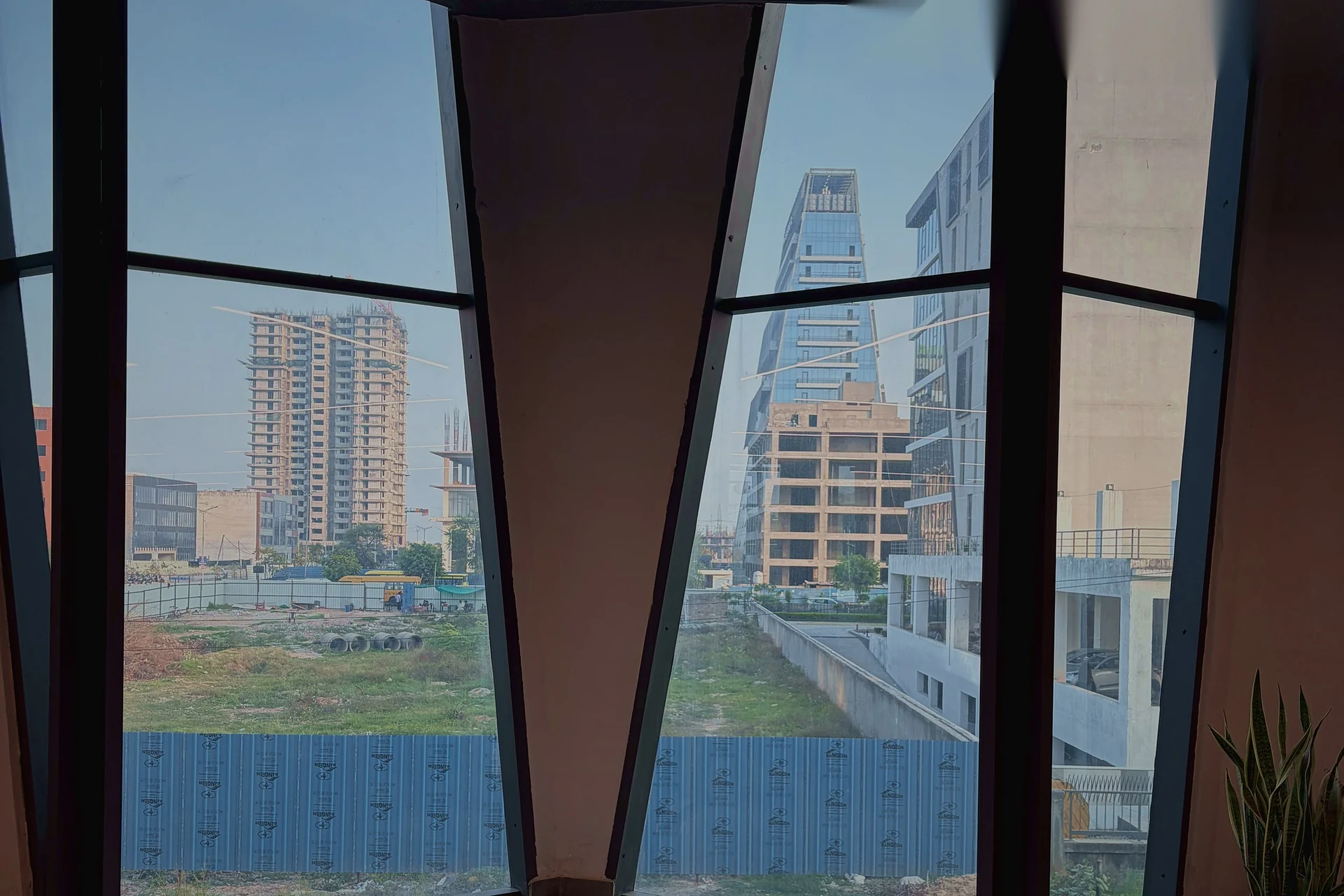 The sawtooth window wall on the Mohali floor, the city rising beyond the glass